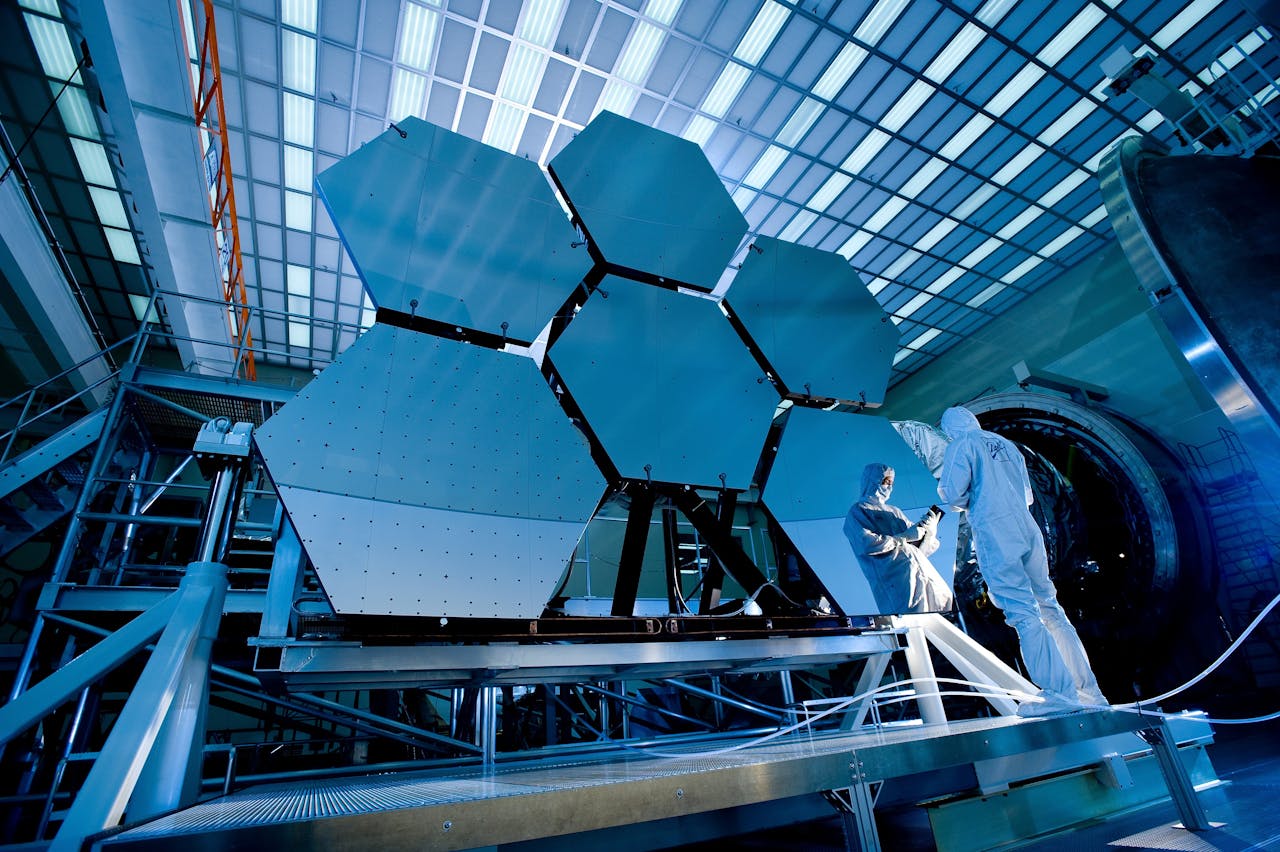 about-02 Engineers in protective suits work on telescopic mirrors in a high-tech lab.