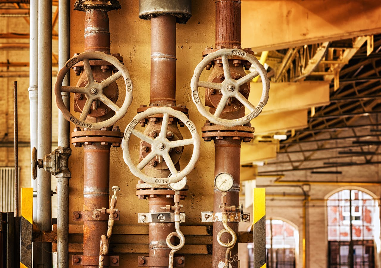 impact-img Close-up of rusty industrial pipes and valves, showcasing aging machinery in a factory setting.