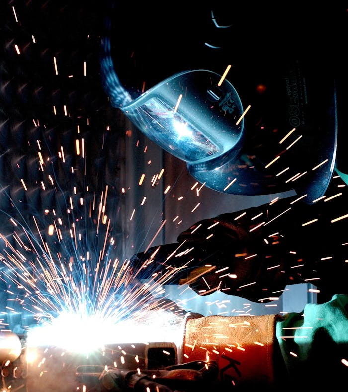 about-01 A focused welder works with metal in an industrial setting, creating vibrant sparks.